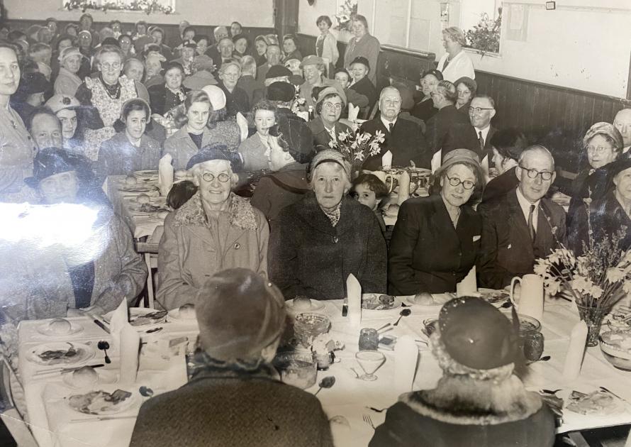 A black and white photo of people sitting at tables for a party in the 1940's.